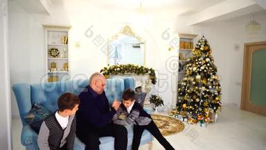 父亲带着孩子玩体育游戏，在圣诞树装饰的房间里坐在蓝色的沙发上玩得很开心